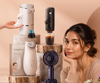 A promotional lifestyle ad featuring a woman in a beige top posing next to a countertop display of home wellness products, including a white facial cleansing device, a black coffee maker, a small purple desk fan, and a boxed skincare item. The background is a soft peach-beige color with text reading 'Better Essentials.